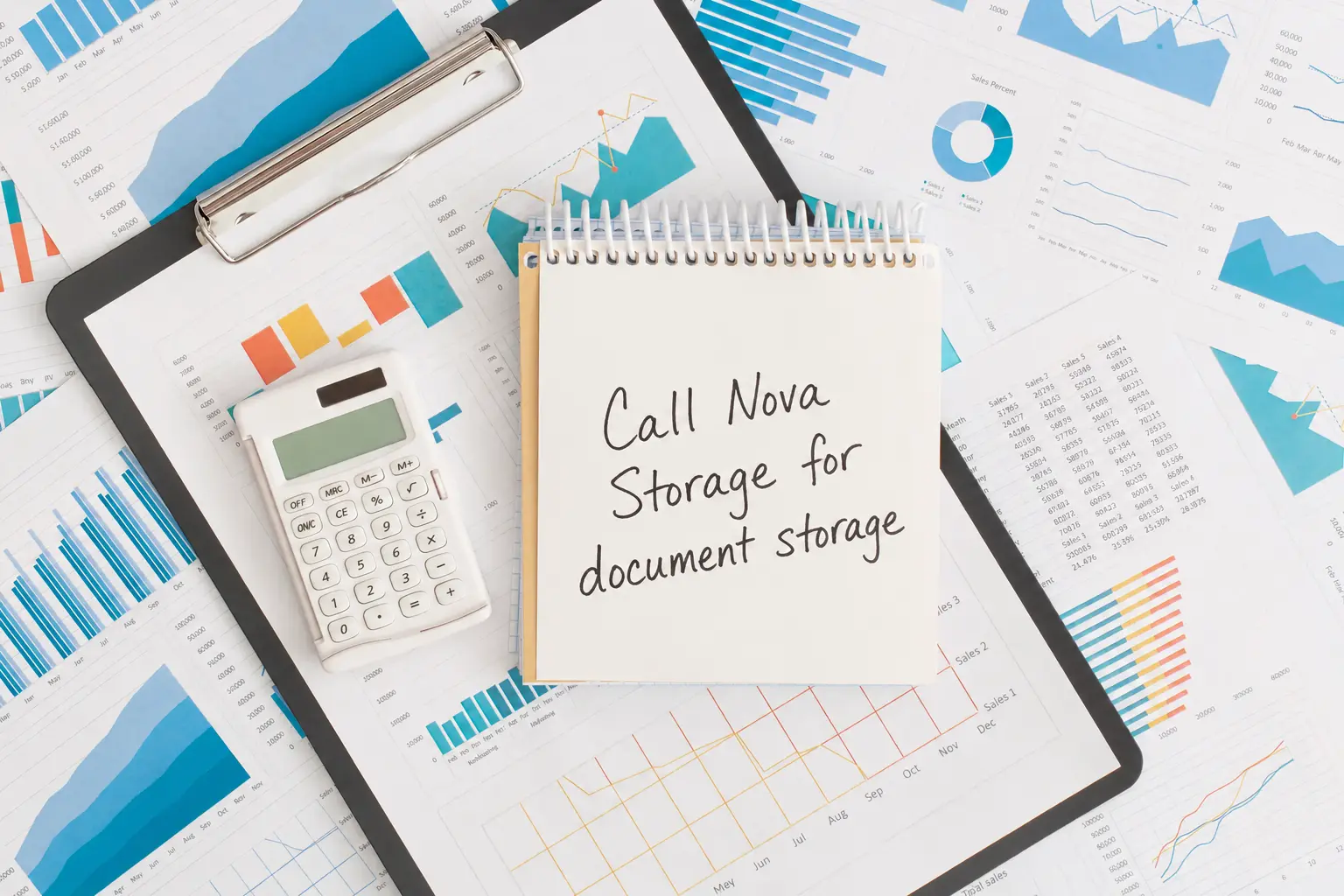 Financial analysis workspace with a clipboard, calculator, notebook, and multiple charts and graphs spread across the desk.